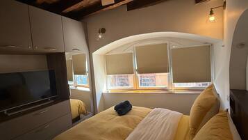 A bedroom with a bed, a television, and a window with blinds.