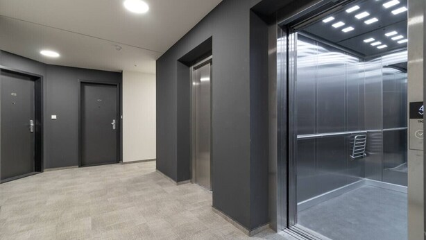 A hallway with three doors, a glass elevator, and a tiled floor. - SMART studio w/1GB speed WiFi + Monitor | A/C | Onsite Free Parking Spot (Praha 5)
