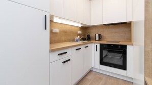 A modern kitchen with white cabinets, a wooden countertop, a built-in oven, and a kettle. - SMART studio w/1GB speed WiFi + Monitor | A/C | Onsite Free Parking Spot (Praha 5)