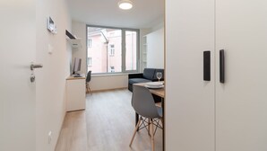 A modern room with a desk, chair, and a window with a view of buildings. - SMART studio w/1GB speed WiFi + Monitor | A/C | Onsite Free Parking Spot (Praha 5)