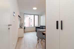 A modern room with a desk, chair, and a window with a view of buildings. - SMART studio w/1GB speed WiFi + Monitor | A/C | Onsite Free Parking Spot (Praha 5)