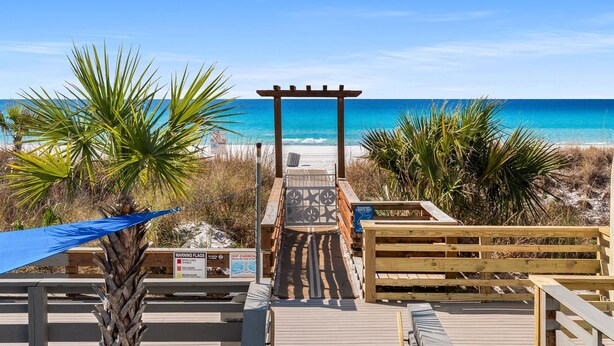 A wooden boardwalk leading to a beach with a pergola and palm trees. - Stylish Boho Studio for 4 | Top of the Gulf Resort (Panama City Beach)