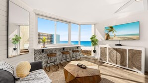 A modern living room with a large window overlooking the beach, a sofa, a coffee table, and a TV on a cabinet. - Stylish Boho Studio for 4 | Top of the Gulf Resort (Panama City Beach)