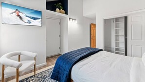 Une chambre à coucher avec un lit, une chaise, un tableau, une porte et une étagère avec des plantes.