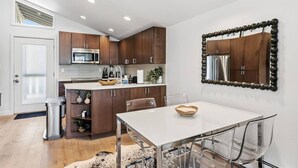 Une cuisine moderne avec des meubles en bois, un réfrigérateur en acier inoxydable et une table à manger blanche, assortie de chaises transparentes.