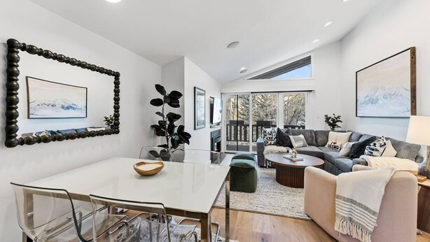 Un salon moderne comprenant un coin repas, un canapé gris et une grande fenêtre laissant entrer la lumière naturelle.