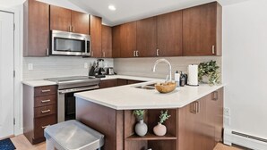 Une cuisine moderne avec des meubles en bois, des appareils en acier inoxydable, un îlot central doté d’un évier et un four à micro-ondes placé au-dessus de la cuisinière.