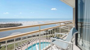 Ein Balkon mit Pool, Liegestühlen und Blick auf Strand und Meer.