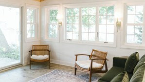 A room with large windows, wooden chairs, a green sofa, and a patterned rug.