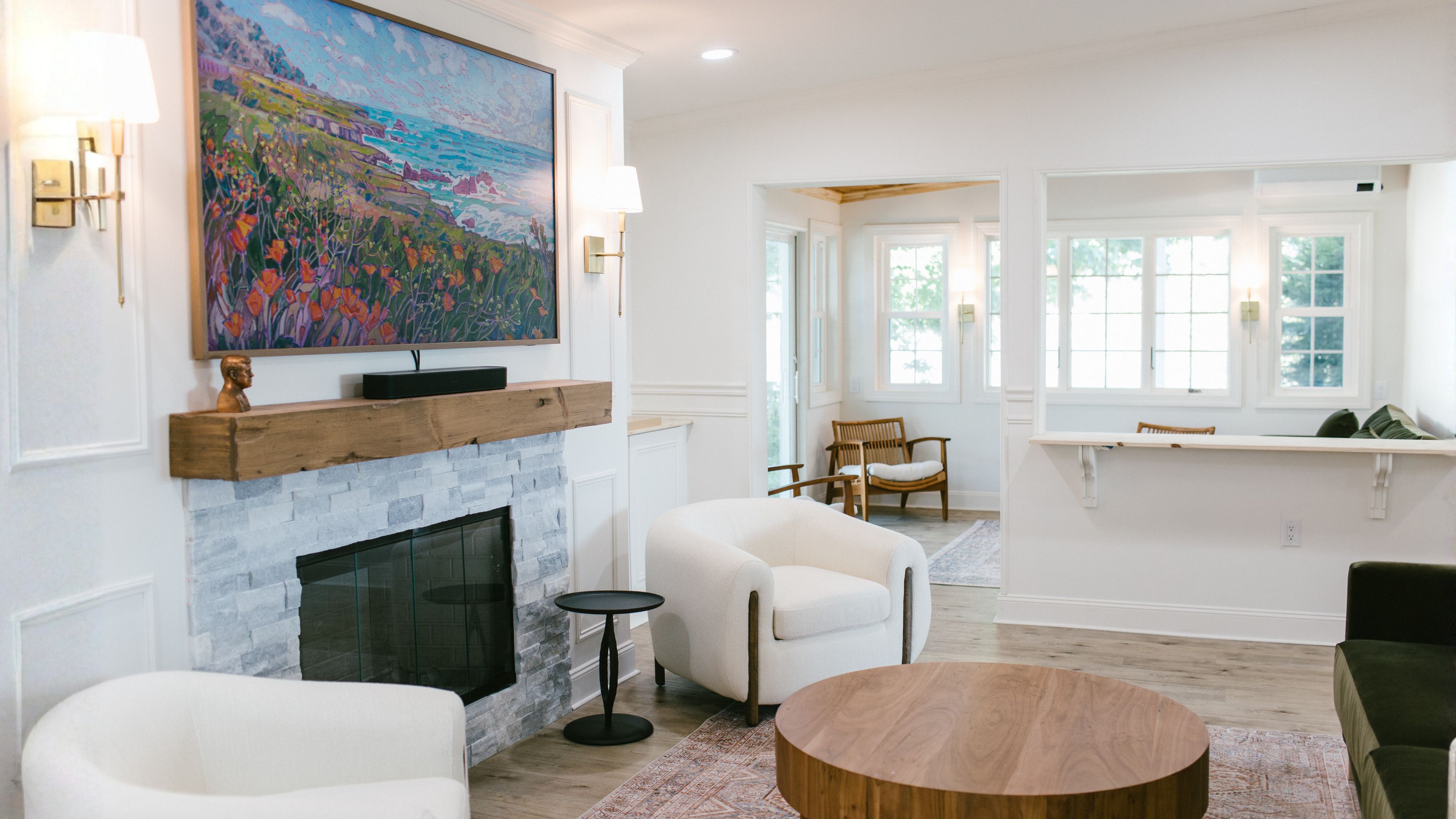 A living room with a fireplace, a large painting, and a view through a window.