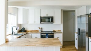 A modern kitchen with white cabinetry, a wooden countertop, a built-in microwave, a stainless steel refrigerator, and a double oven.