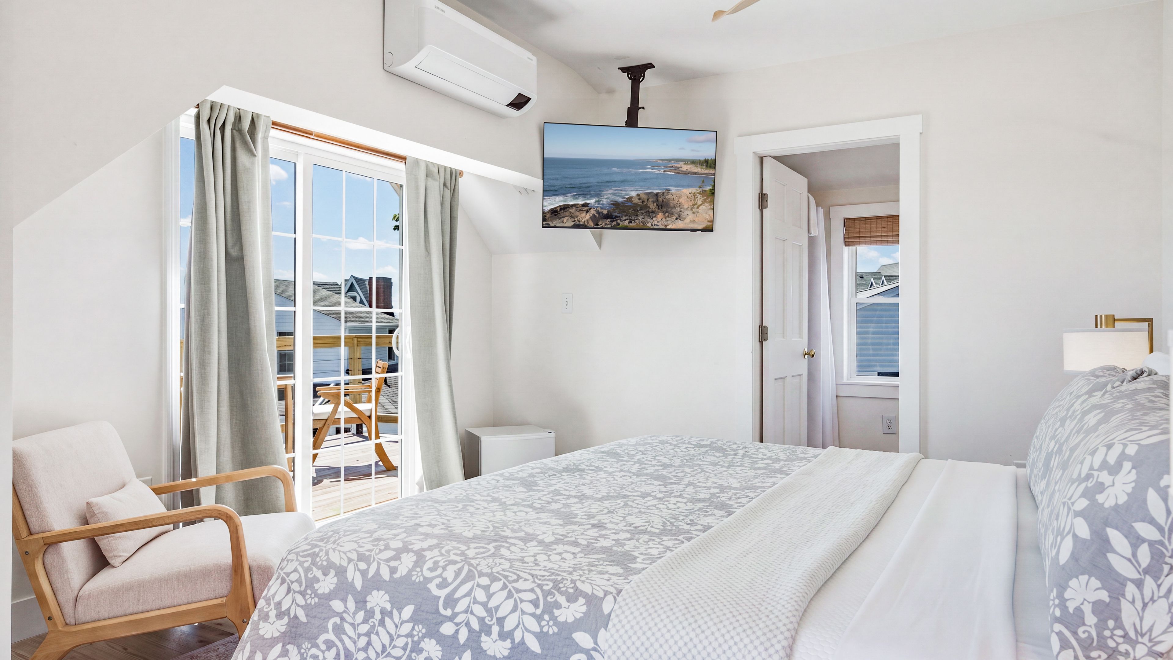 A bedroom with a bed, a chair, a TV, and a view of the outdoors.