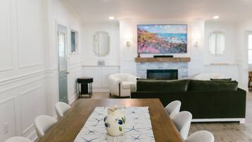A dining area with a wooden table, chairs, a vase, and a painting above the fireplace.