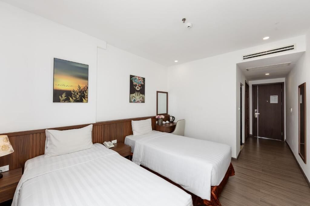 A hotel room with two single beds, a bedside table with a lamp, a mirror, and artwork on the wall.