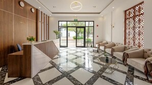 Um saguão de hotel com balcão de recepção, área de estar e uma grande porta de vidro que dá para o exterior.