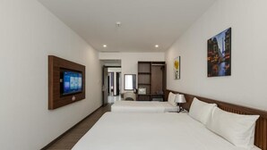 Quarto de hotel com uma cama grande, televisão fixada na parede, secretária com cadeira e guarda-roupa.
