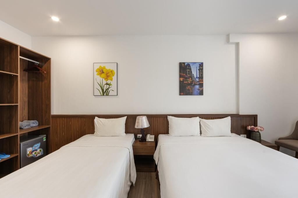 A hotel room with two beds, a wooden wardrobe, a nightstand with a lamp, and two framed pictures on the wall.