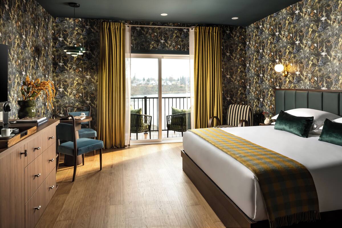 Habitación de hotel con una cama grande, un escritorio con una silla, vistas al exterior a través de una puerta corredera y un balcón.