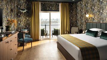 Habitación de hotel con una cama grande, un escritorio con una silla, vistas al exterior a través de una puerta corredera y un balcón.