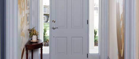 A room with a white door, wooden floor, and a small table with a vase.