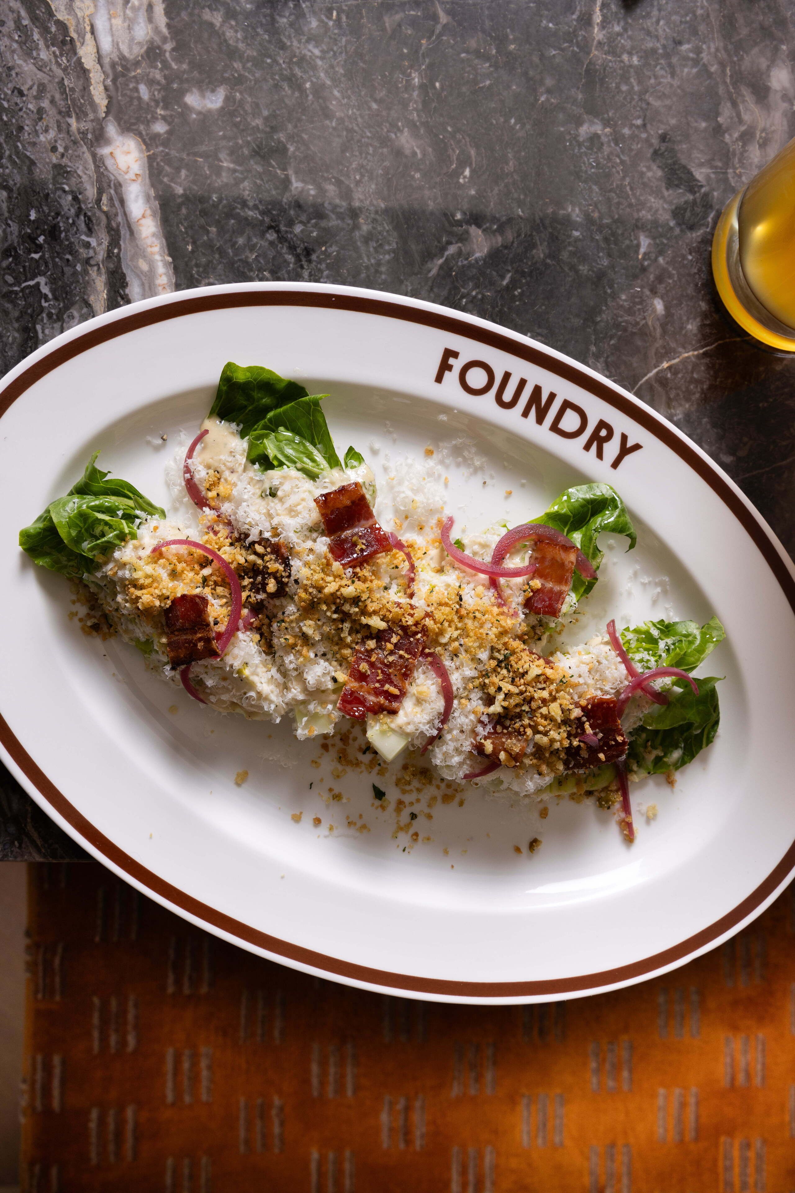 Een bord eten met daarop de tekst 'FOUNDRY', geplaatst op een tafel met een patroon doek.