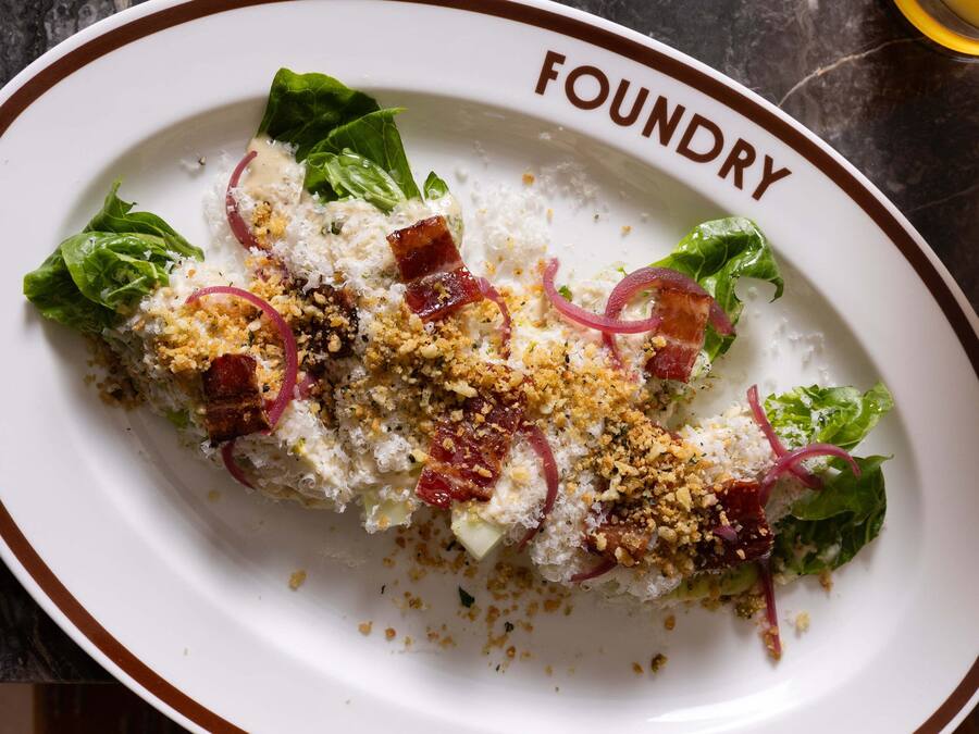 Een bord eten met daarop de tekst 'FOUNDRY', geplaatst op een tafel met een patroon doek.