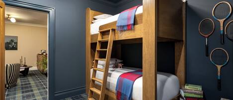A bunk bed with a wooden ladder, a bookshelf with travel books, and a tennis racket wall art.