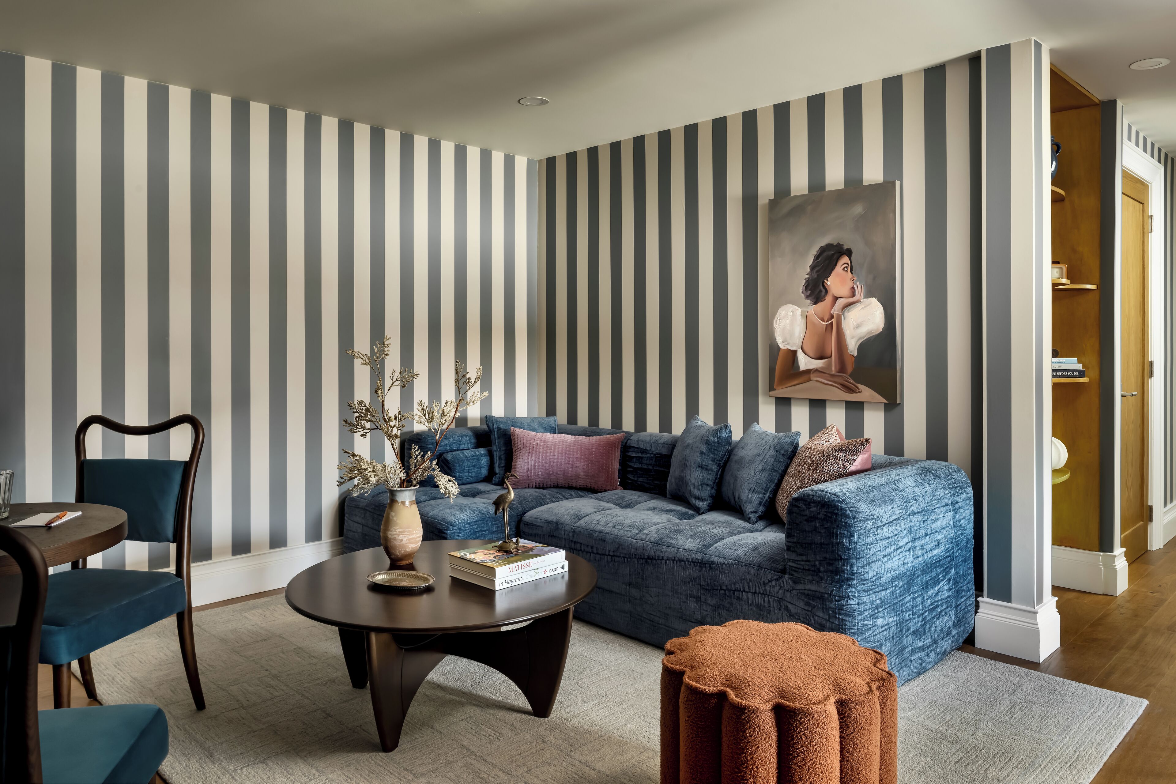 A modern living room with a striped wall, a blue sofa, a coffee table, and a painting.