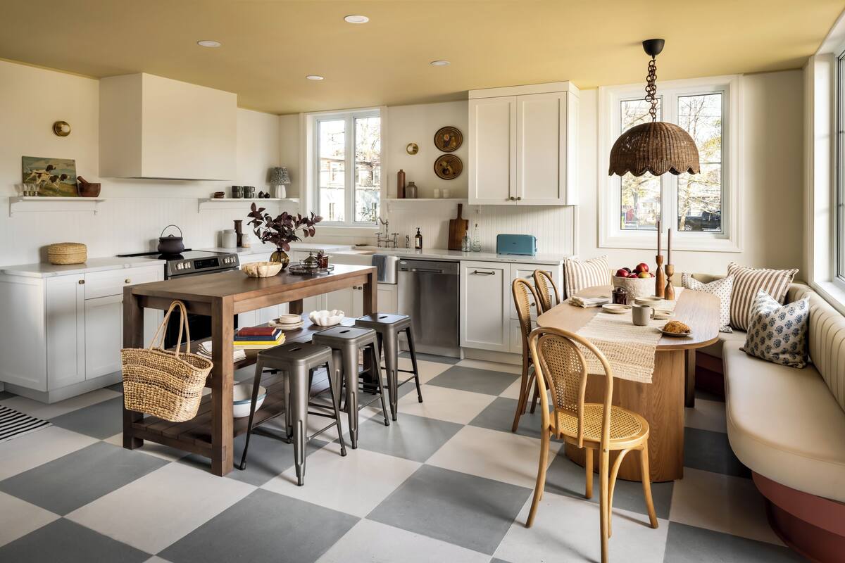 Una cocina moderna con armarios blancos, un comedor con piso a cuadros y una sala de estar con sofá y cojines.