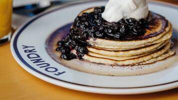 Une pile de crêpes garnies de myrtilles et surmontées de crème fouettée, le tout présenté sur une assiette où est inscrit le mot « FAMILLE ».