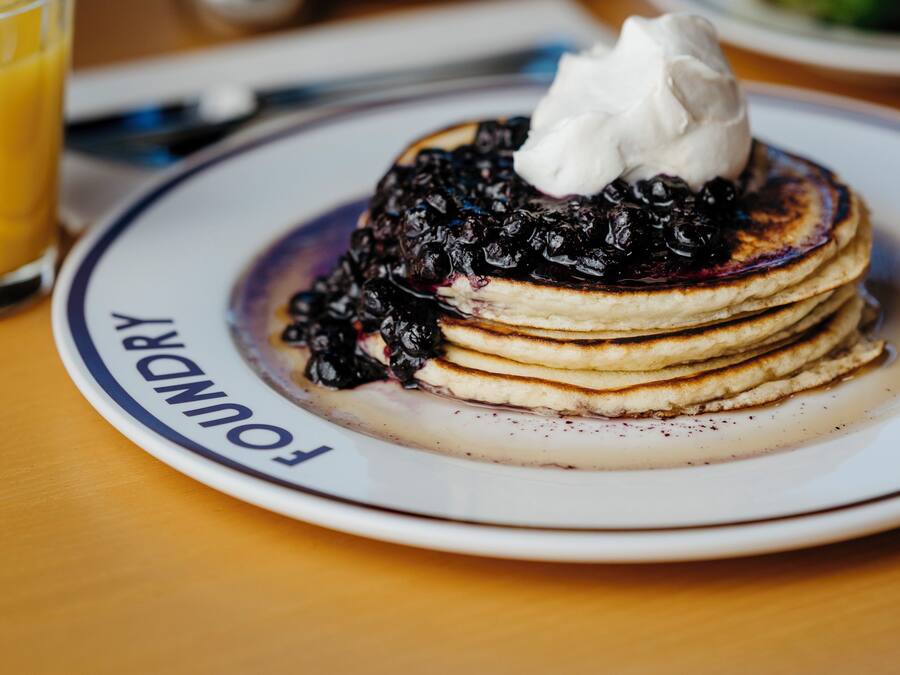 Une pile de crêpes garnies de myrtilles et surmontées de crème fouettée, le tout présenté sur une assiette où est inscrit le mot « FAMILLE ».
