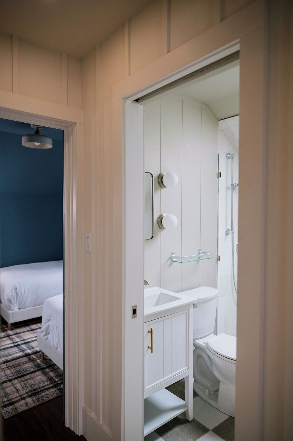 Una habitación con una cama, un baño blanco con lavamanos e inodoro, y una pared azul.