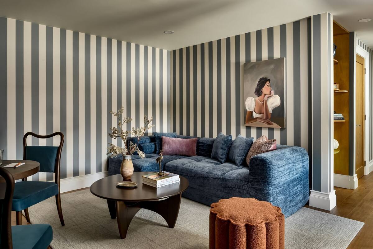 Una sala de estar con pared a rayas, un sofá, una mesa de centro y un cuadro.