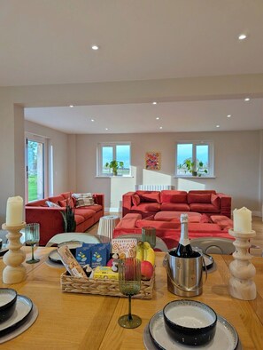 A spacious living room with a red sofa set, a dining table with candles, a bottle of champagne, and a basket of bread.