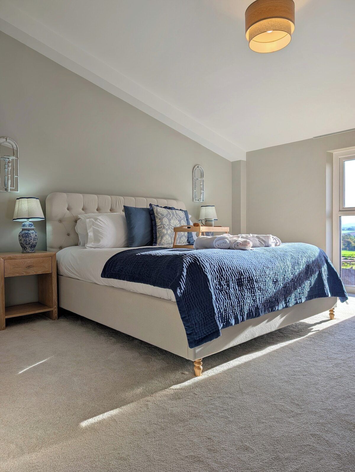 A bedroom with a bed, nightstands, a hanging light fixture, and a window.