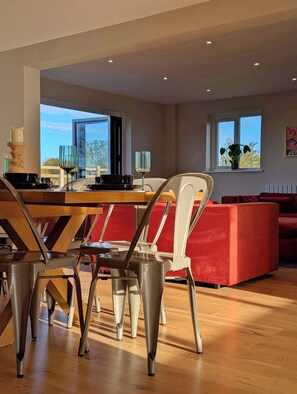 A modern dining area with a wooden table and metal chairs, a red sofa, and a view of the outdoors through large windows.