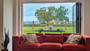 A red sofa with cushions, a potted plant, and a table with a vase and cups. - The Gathering Barn | Hot Tub | Sleeps 12 | Luxury Countryside Views | (Hereford)