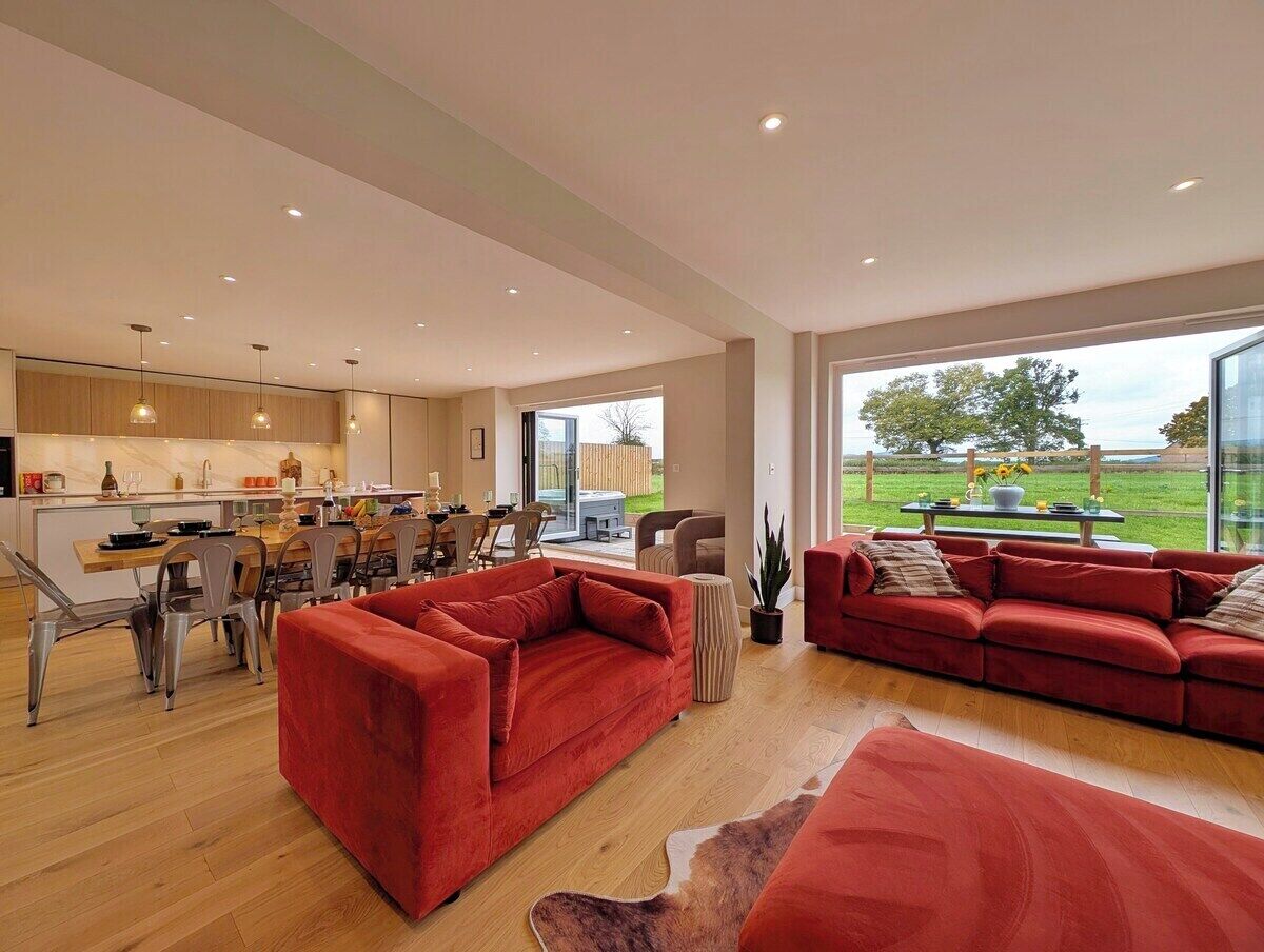 Amplia sala de estar con un sofá rojo, una mesa de comedor con sillas y una cocina al fondo.