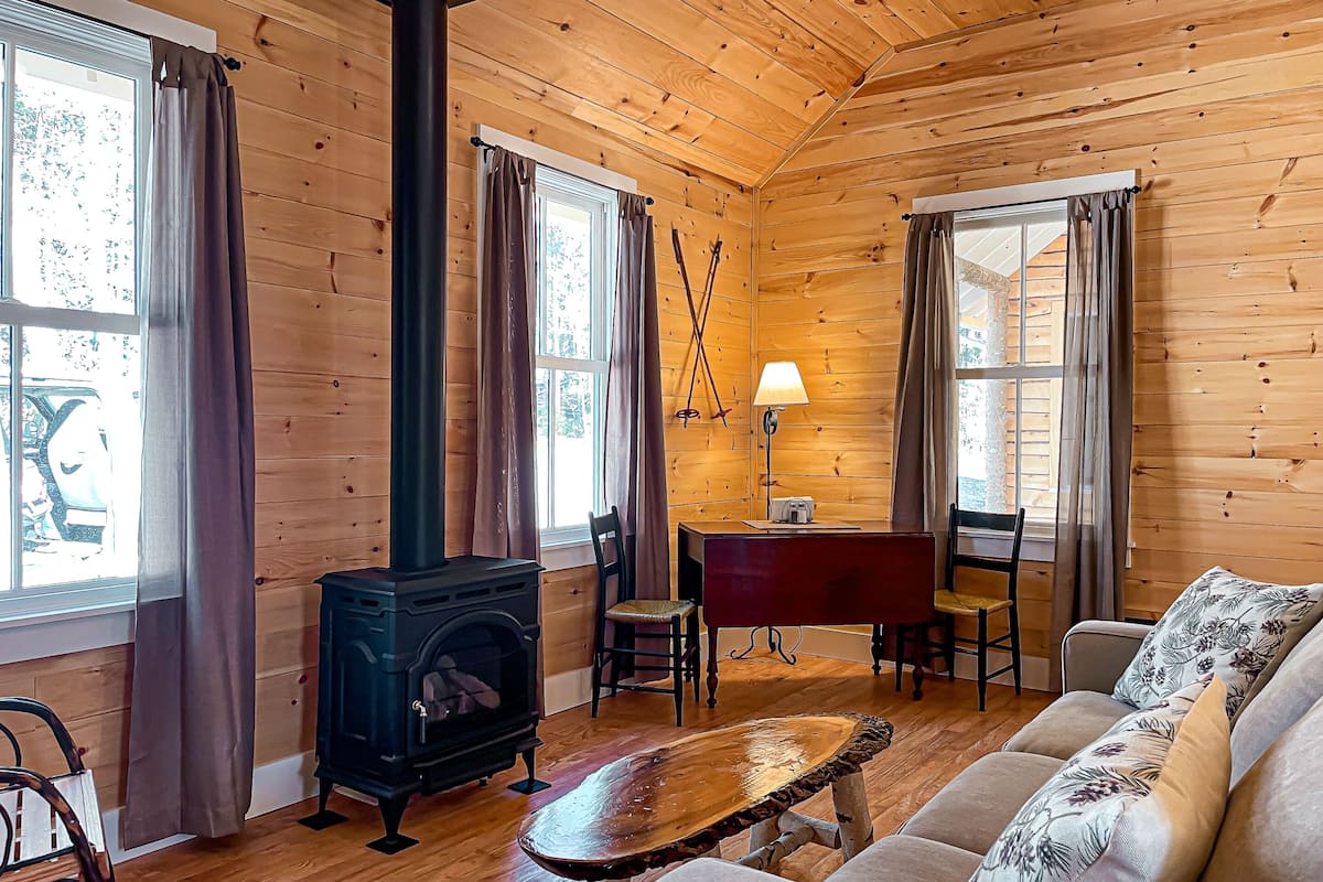 Una cabaña acogedora con estufa de leña, paredes de madera, un sofá y comedor.