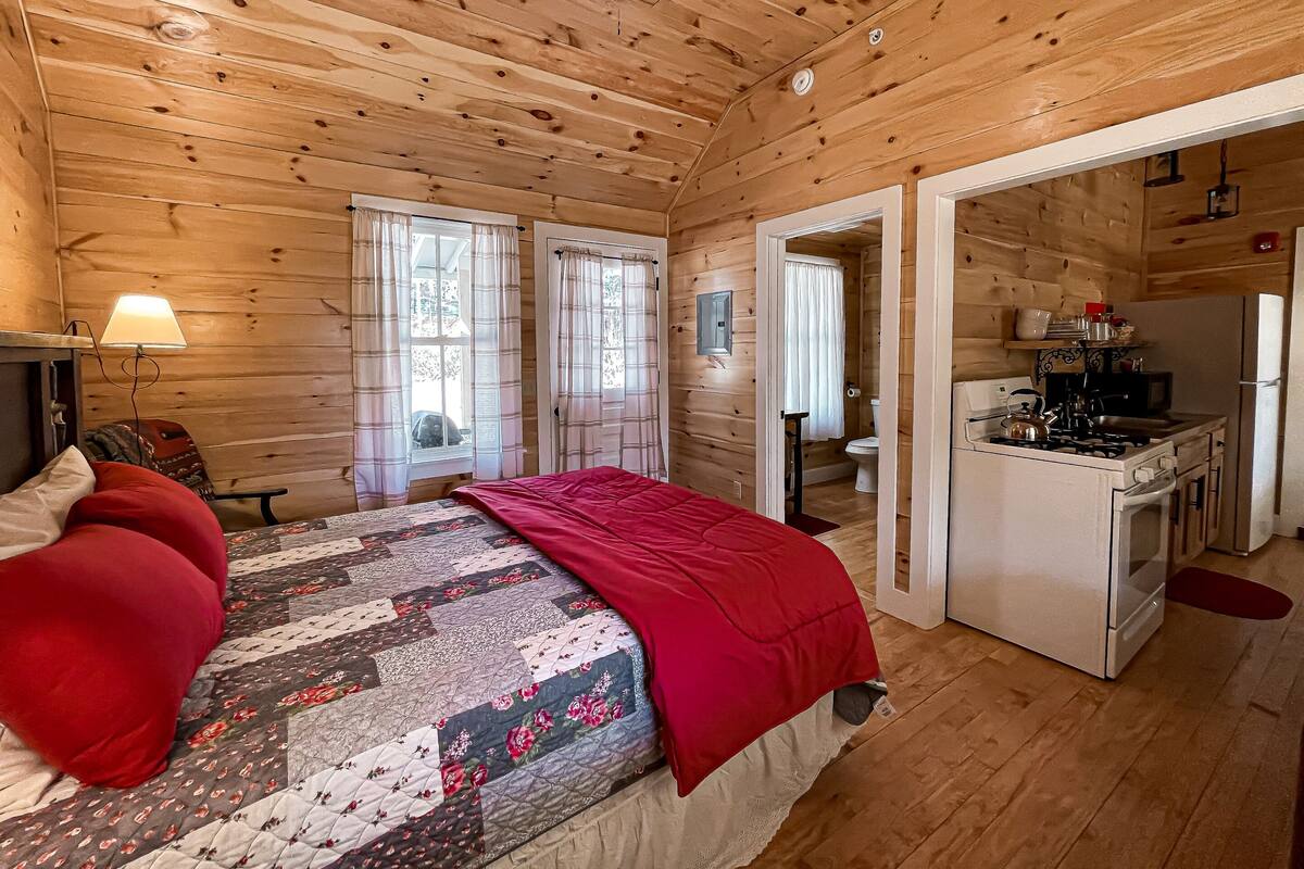 Una habitación de cabaña de madera con una cama, un escritorio y un pequeño espacio para cocinar.