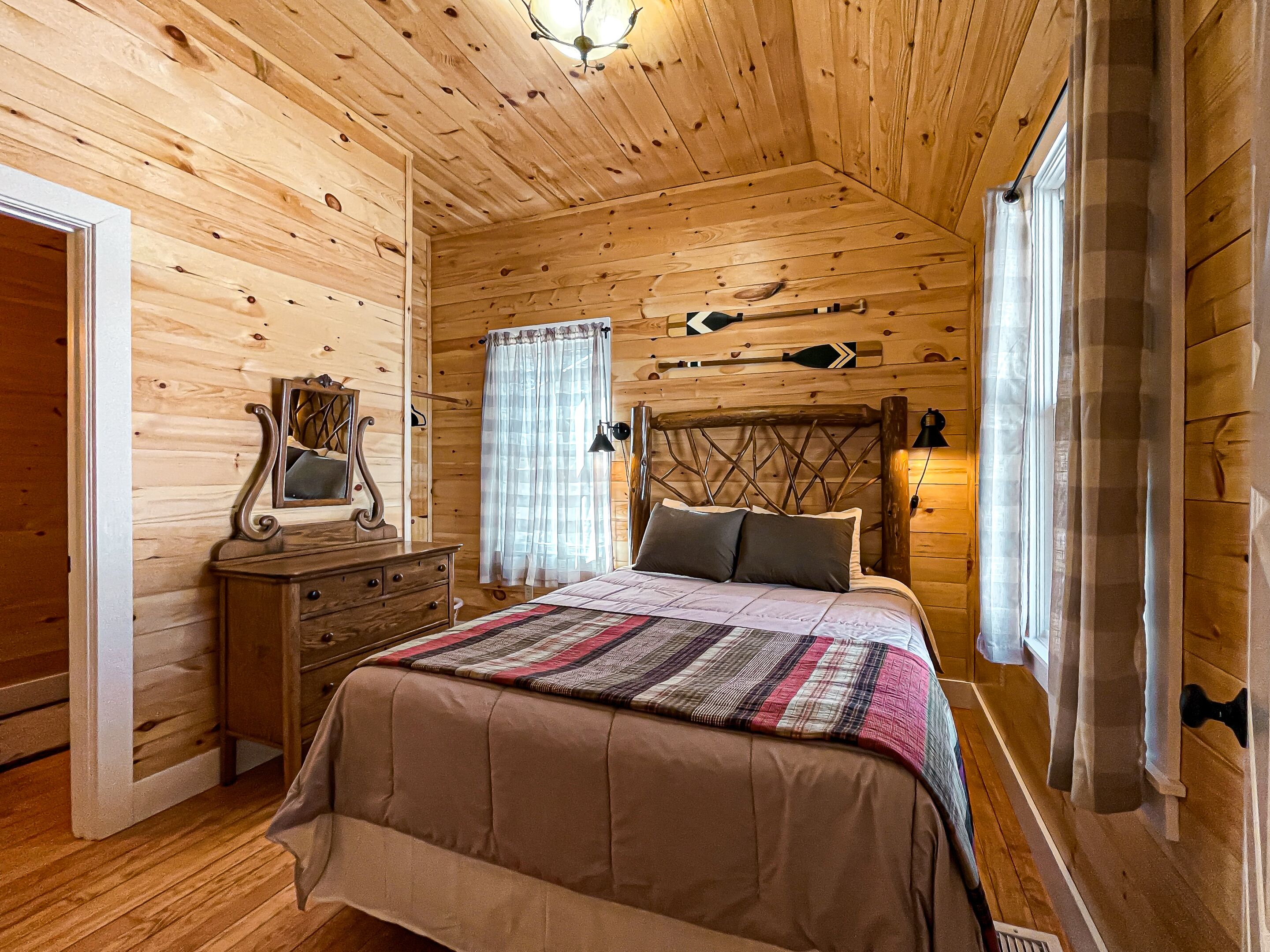 A cozy wooden cabin bedroom with a bed, dresser, and a mirror.
