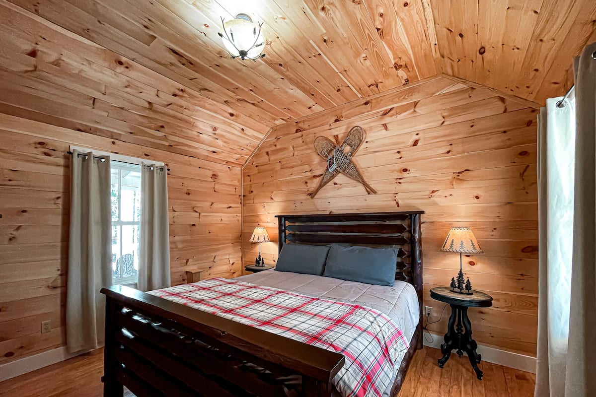 Un dormitorio con paneles de madera, una cama, dos lámparas de noche, una pequeña mesa y una estrella decorativa en la pared.