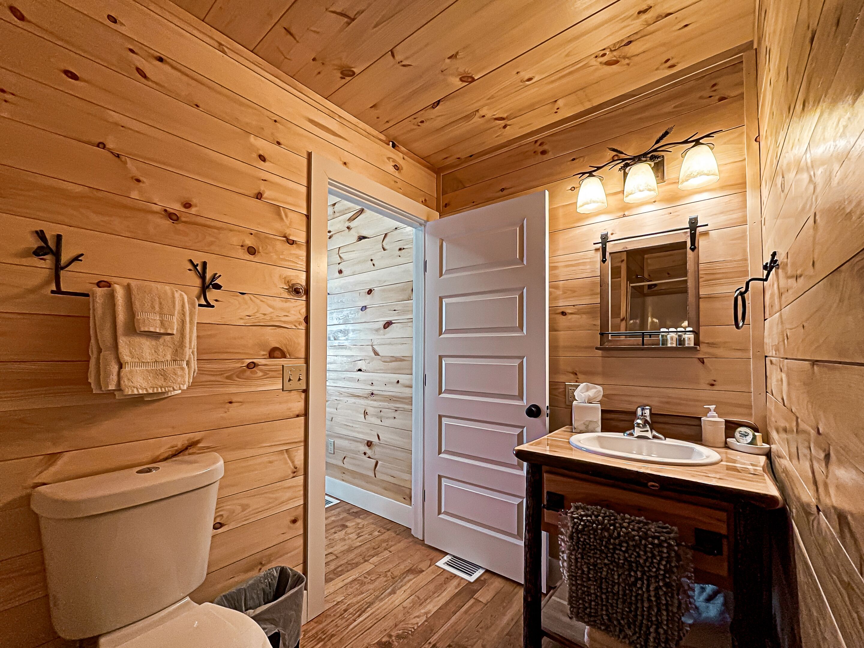 A wooden cabin bathroom with a toilet, sink, and mirror.