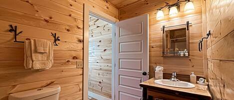 A wooden cabin bathroom with a toilet, sink, and mirror.