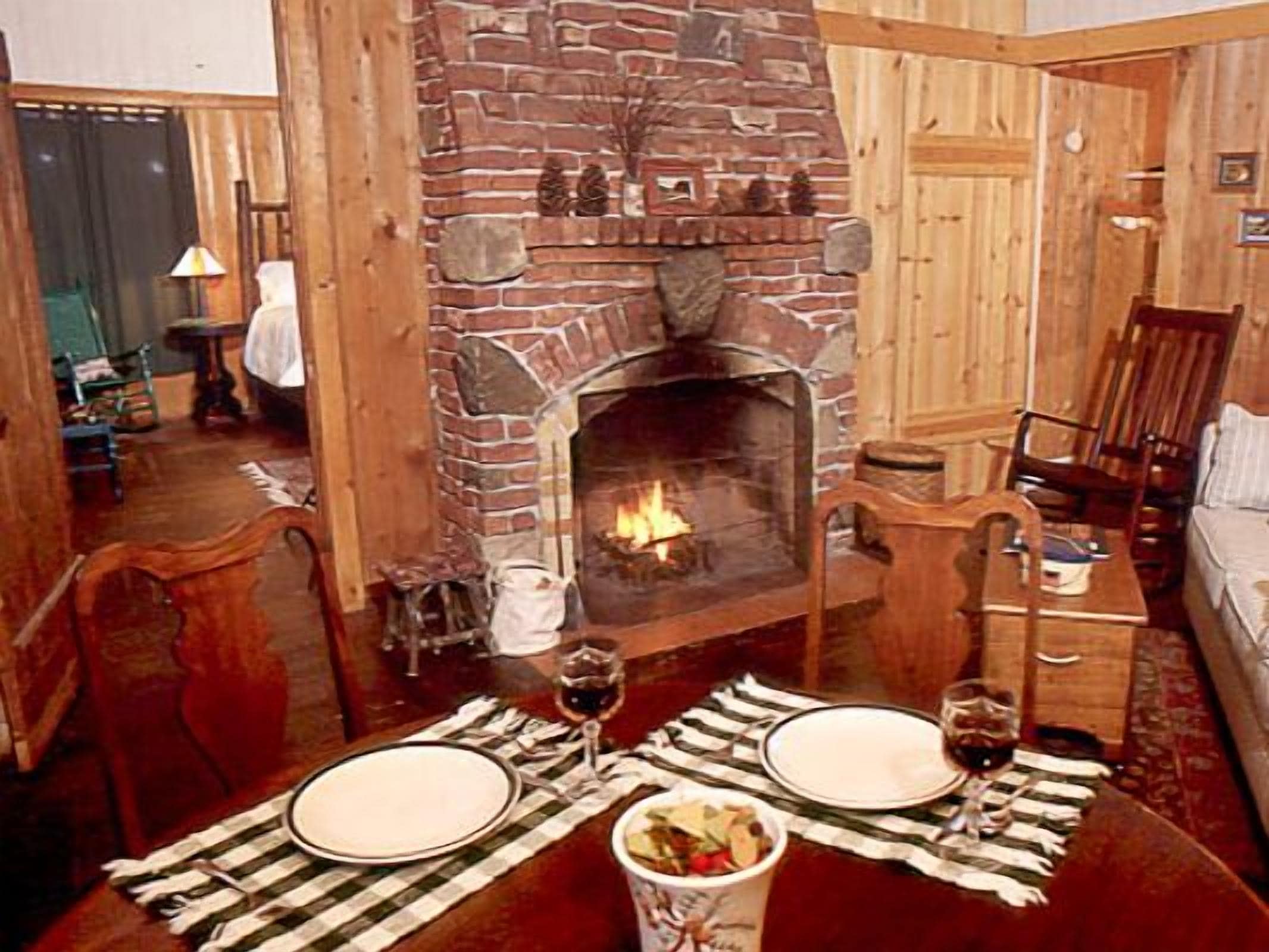 A cozy room with a brick fireplace, wooden furniture, and a dining table set for two.