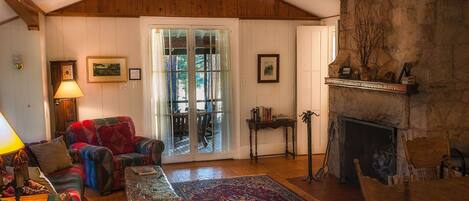 A cozy living room with a fireplace, wooden ceiling, and a large window.