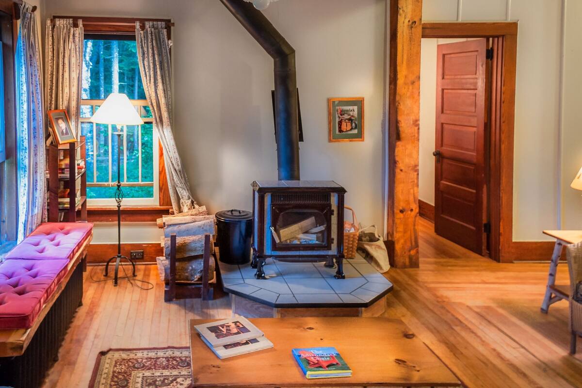 Una sala de estar acogedora con chimenea, un sofá, una mesa con libros y una ventana con cortinas.