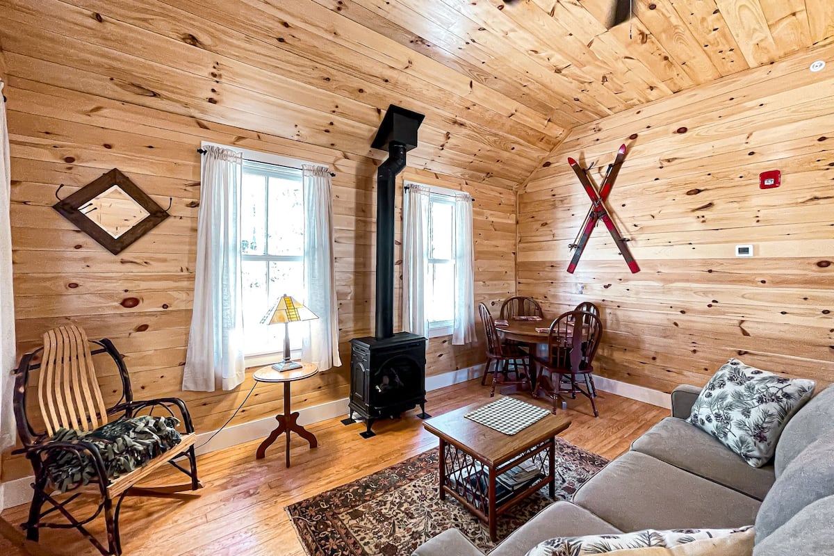Interior acogedor de una cabaña con paredes de madera, chimenea, sofá, mesa de comedor y una silla.