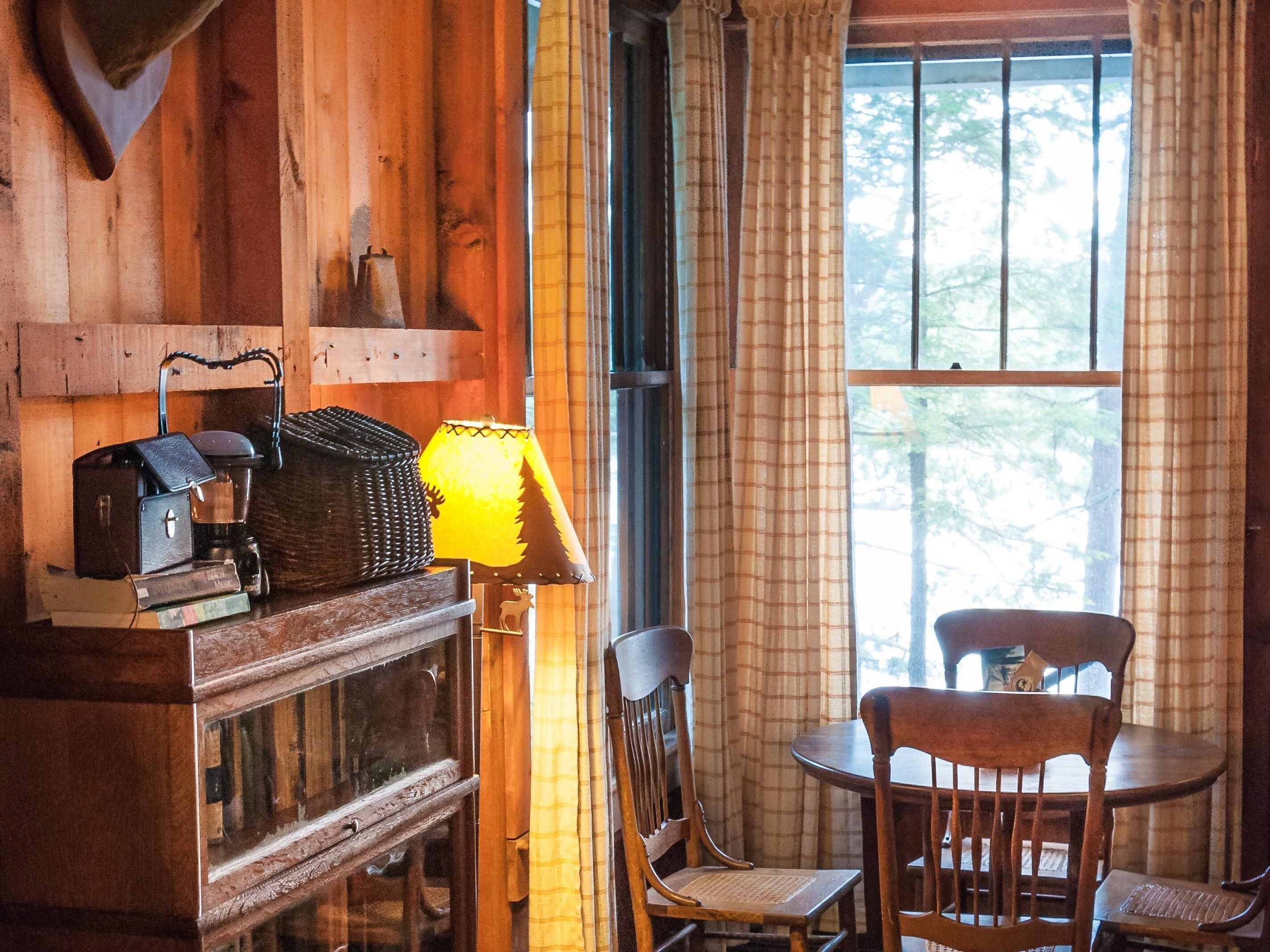 Una habitación acogedora con detalles de madera, una mesa con sillas, una lámpara y un ventanal con cortinas.