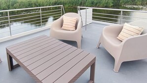 Une terrasse avec une table et deux chaises, donnant sur une étendue d’eau calme.